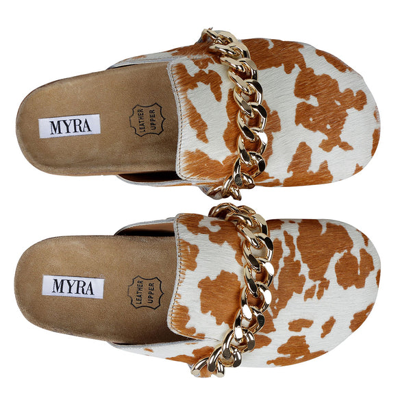 Brown and white cowhide slip-on slippers with golden chain detailing on the upper